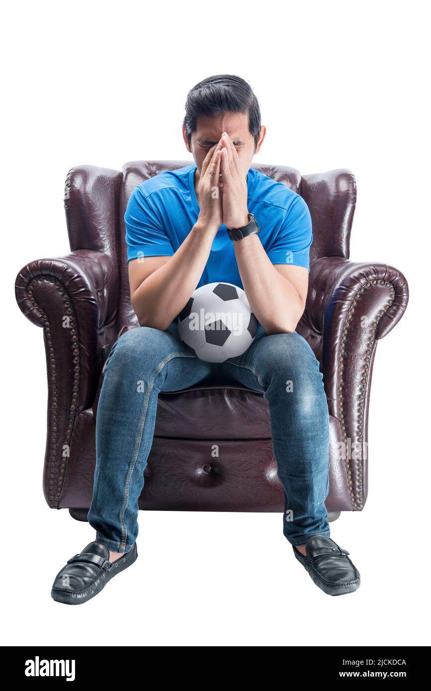 Asian man with the ball sitting on the couch with a disappointed expression isolated over white background Stock Photo