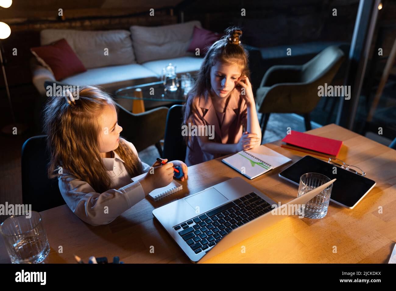 Live portrait of cute kids, sisters sitting at home play computer games ...