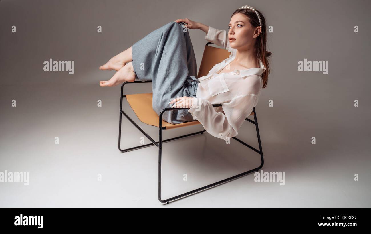 Feet up. Casual young woman sits barefoot on a comfortable armchair, relaxes, raises her legs Stock Photo