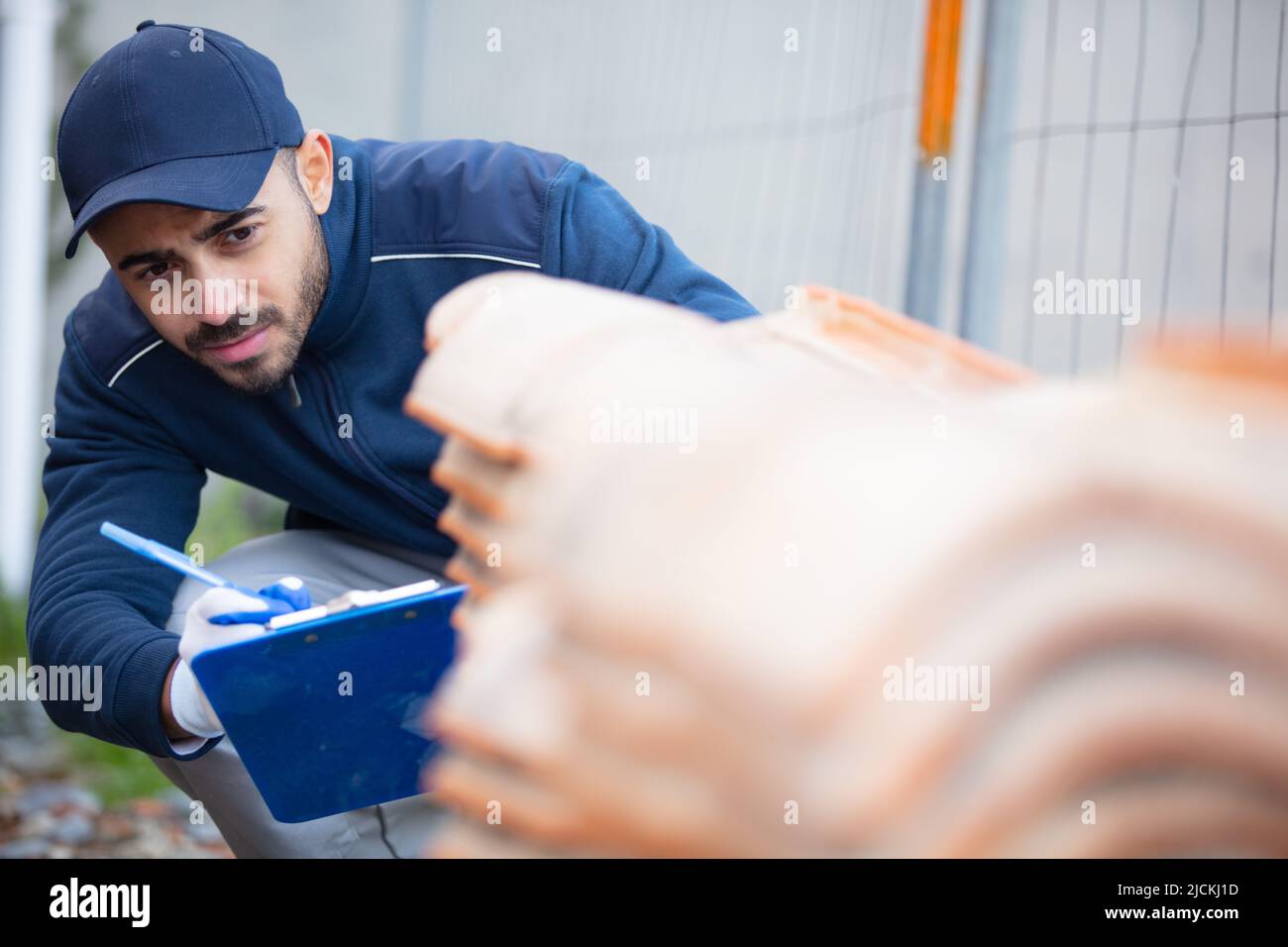 man with clipboard inspects stack of roof tiles Stock Photo