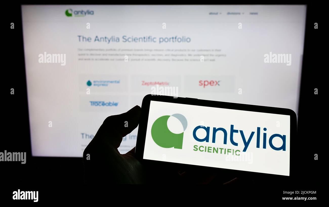 Person holding smartphone with logo of US biotechnology company Antylia Scientific on screen in front of website. Focus on phone display. Stock Photo