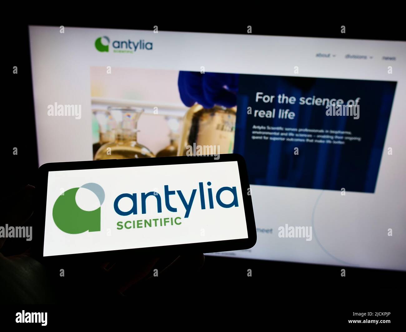 Person holding mobile phone with logo of American biotechnology company Antylia Scientific on screen in front of web page. Focus on phone display. Stock Photo