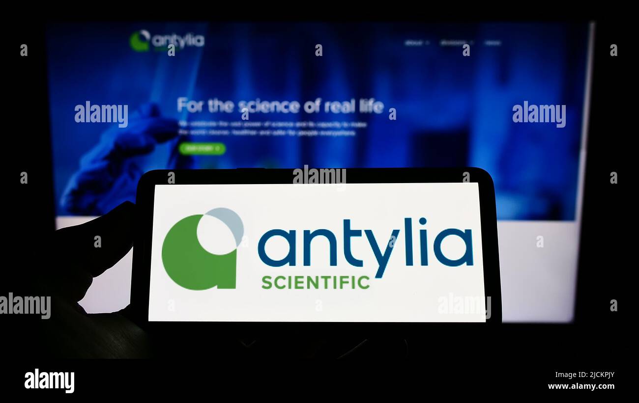 Person holding cellphone with logo of US biotechnology company Antylia Scientific on screen in front of business webpage. Focus on phone display. Stock Photo