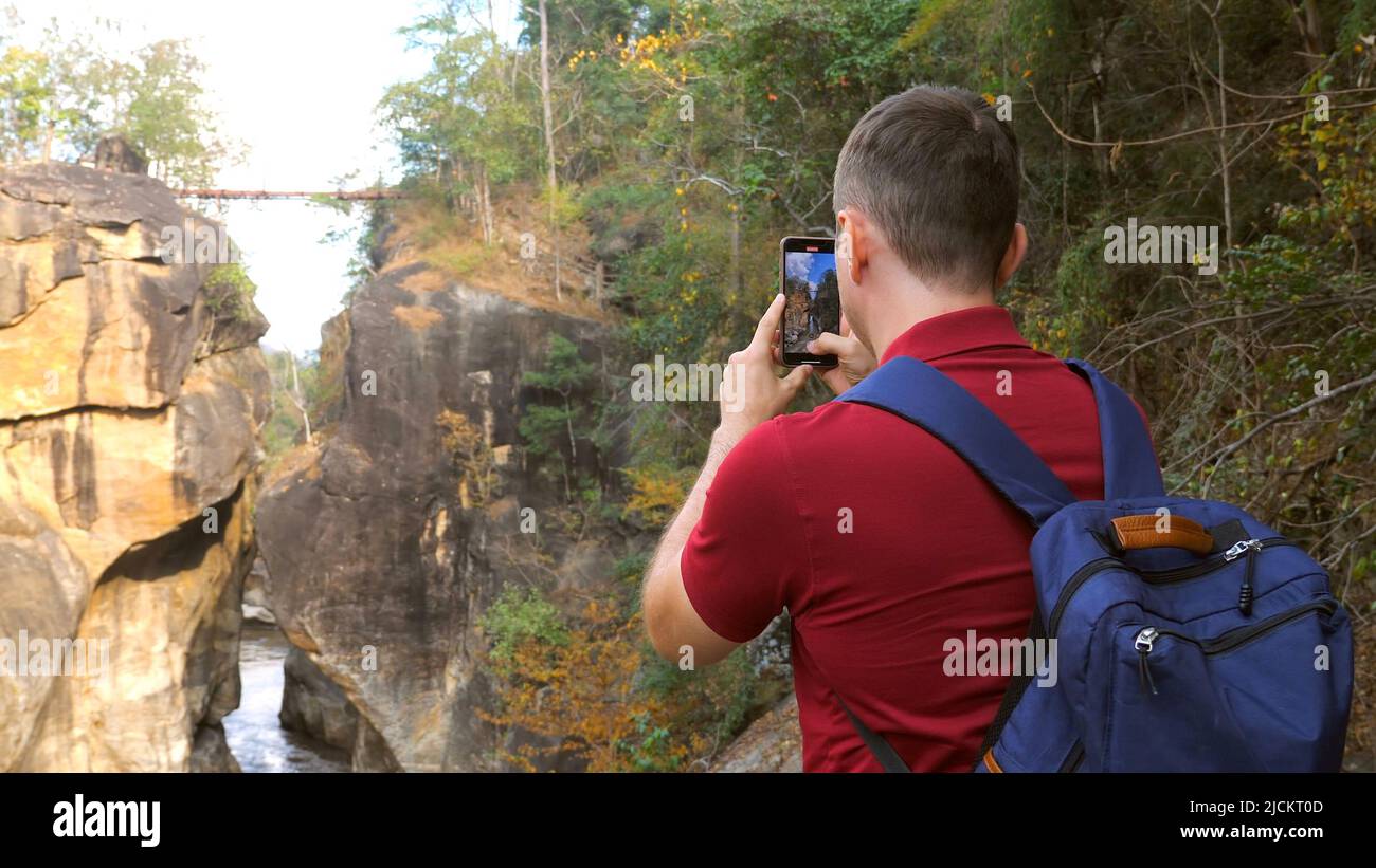 Casual travel blogger shooting video of amazing nature in national park in Thailand. Back view of 30s forest hiker photographer man with backpack make Stock Photo