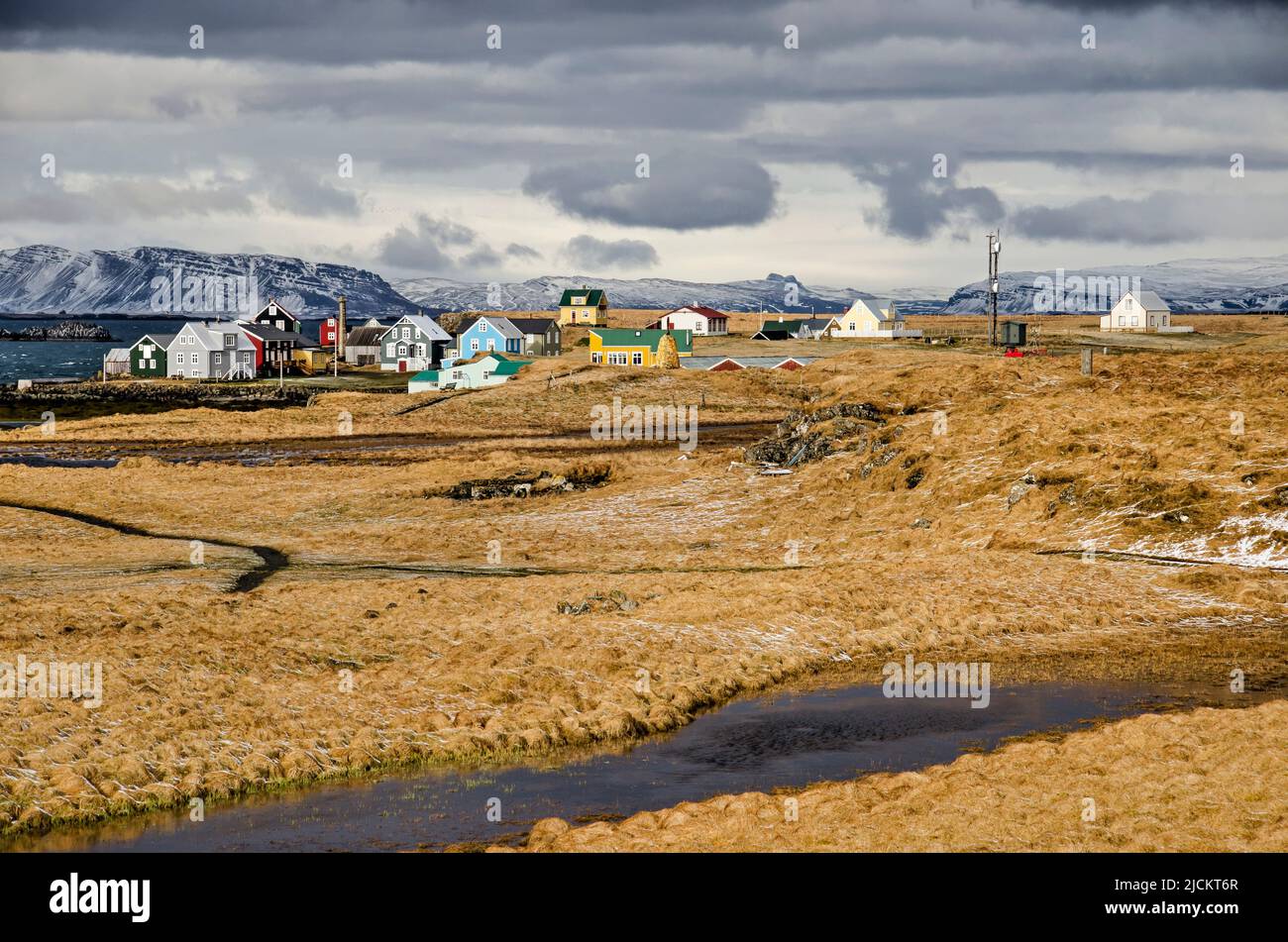 Flatey, Iceland, May 5, 2022: view across the yellow-brown fields, partly snow-covered, towards the village and the fjord and mountains beyond Stock Photo