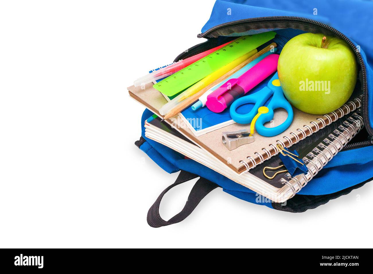 The students blue open schoolbag is filled with notebooks, pens, markers, stationery and a green apple lies on its side, isolated on white background. Stock Photo