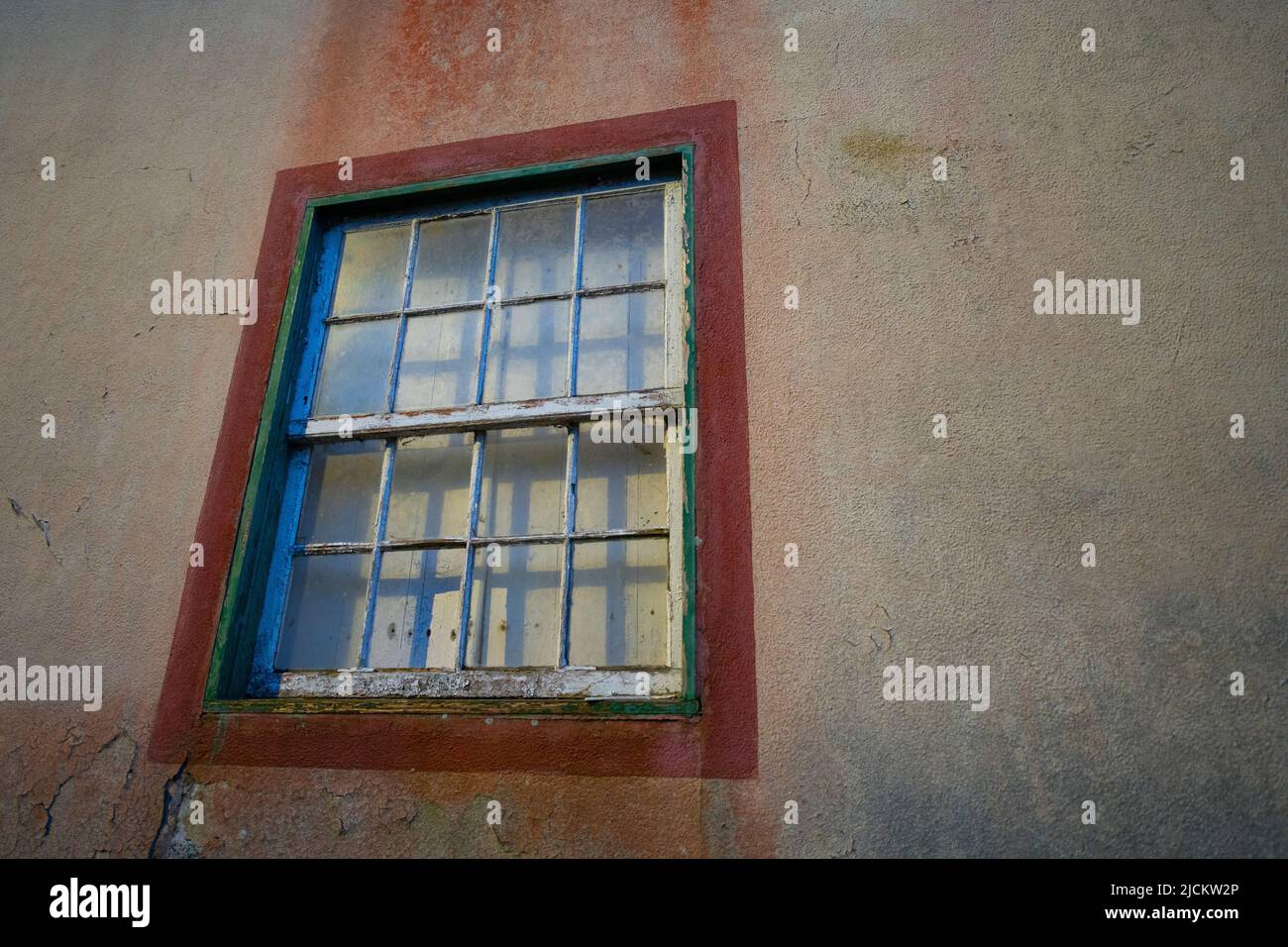 old antique wooden window frame around window in concrete exterior wall of urban home white wood pane frames with peeling paint curtain pulled closed Stock Photo