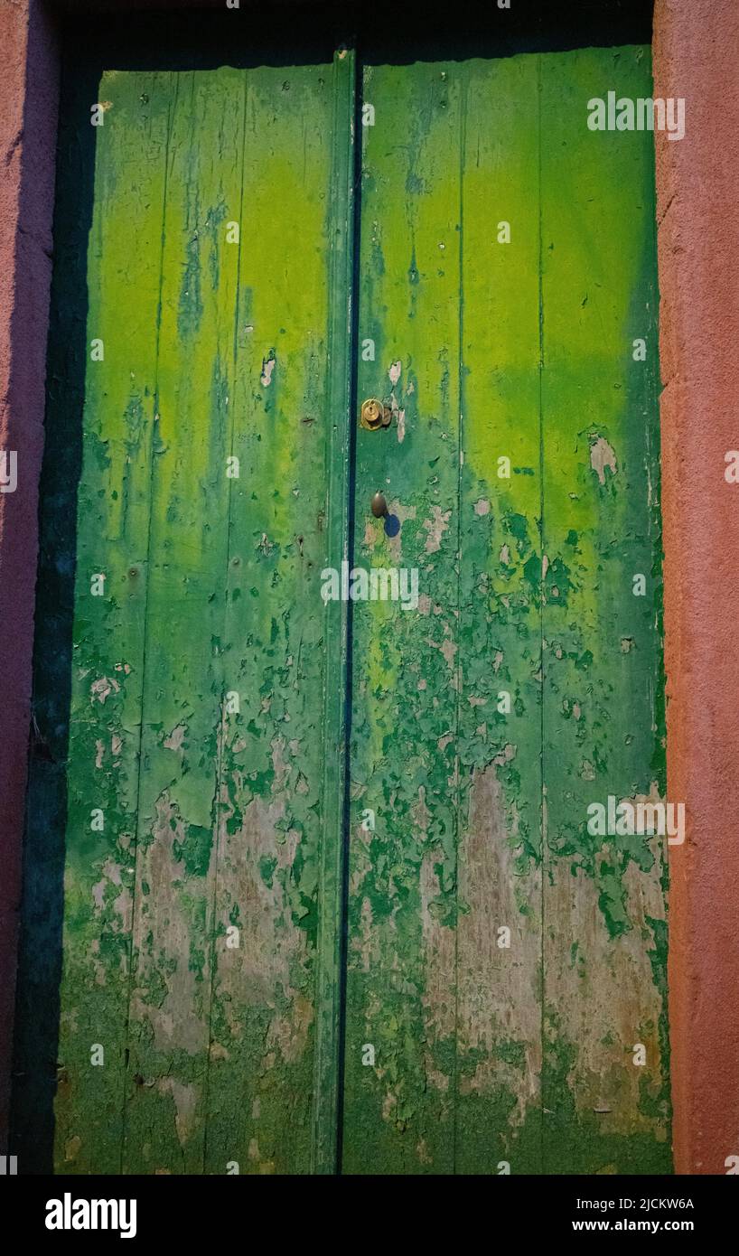 old weathered green wooden doors paint peeling and fading exterior doors of old house in the Azores of Portugal on the island of faial vertical format Stock Photo