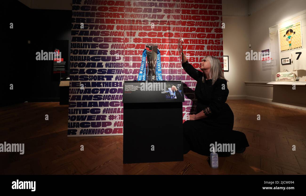 Brighton, UK. 14th June, 2022. Head of Exhibitions Helen Grundy polishes the cabinet containing the Barclays FA Women's Super League Trophy which forms part of the Goal Power Women's football Exhibition at the Brighton Museum & Art Gallery. Credit: James Boardman/Alamy Live News Stock Photo