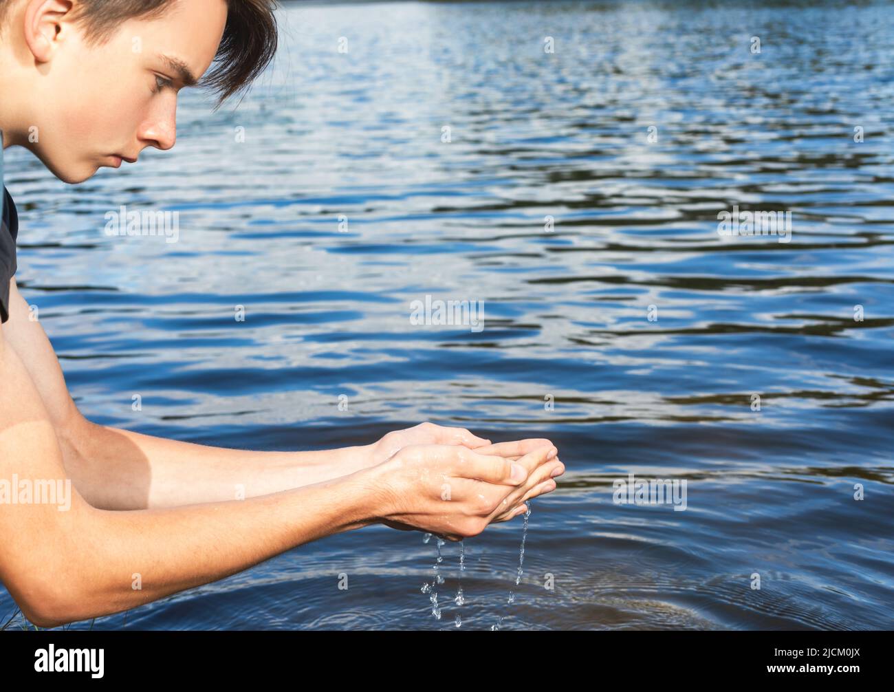 Teenage boy scoops up raw water from a lake. Natural water resources environmental awareness concept Stock Photo