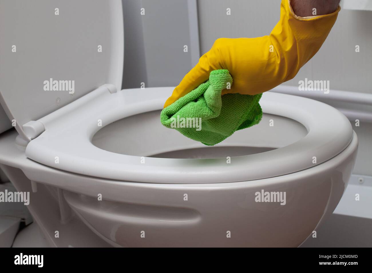 Man wearing glove cleaning toilet bowl in bathroom, closeup Stock Photo