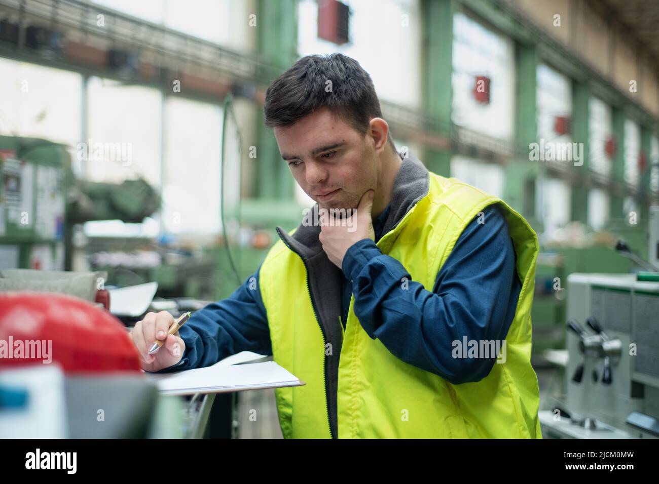 Young man with Down syndrome working in industrial factory, social integration concept. Stock Photo