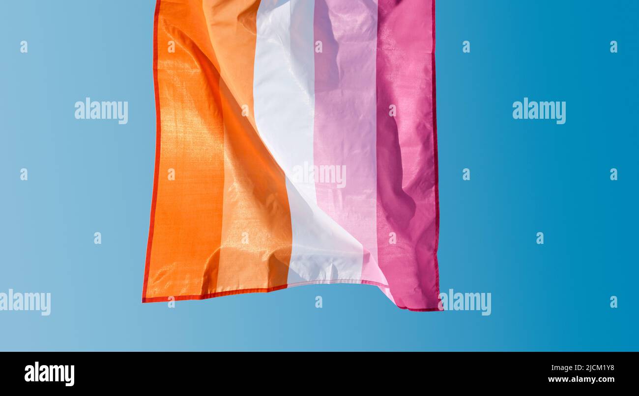 closeup of a lesbian pride flag, seen from behind, waving in the wind against the sky in a sunny day Stock Photo