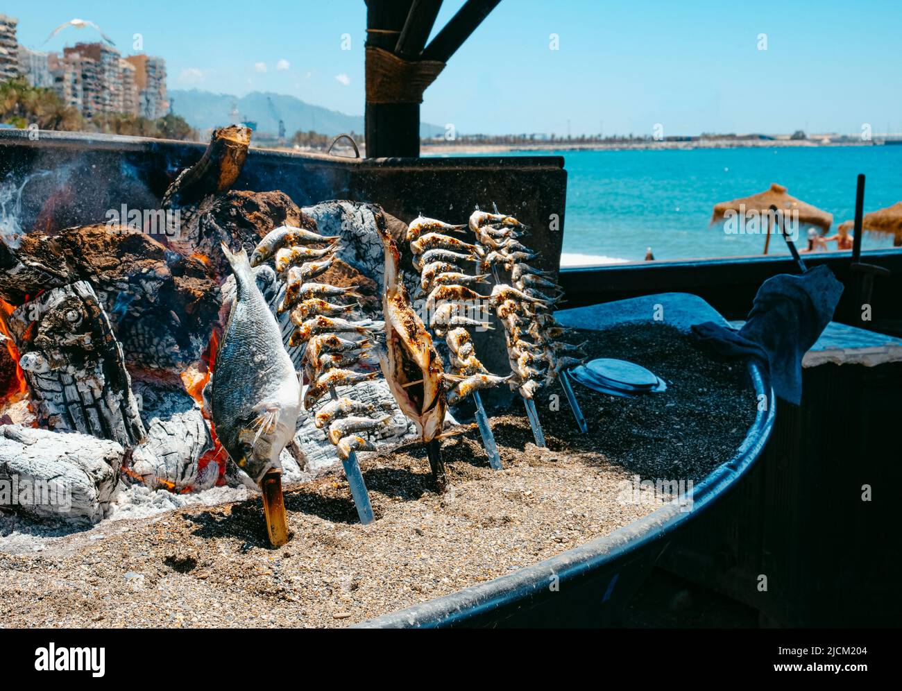 closeup of some espetos, a kind of skewers where fish is skewered, beeing cooked in a wood fire, as is traditional in Malaga, in La Malagueta beach, M Stock Photo
