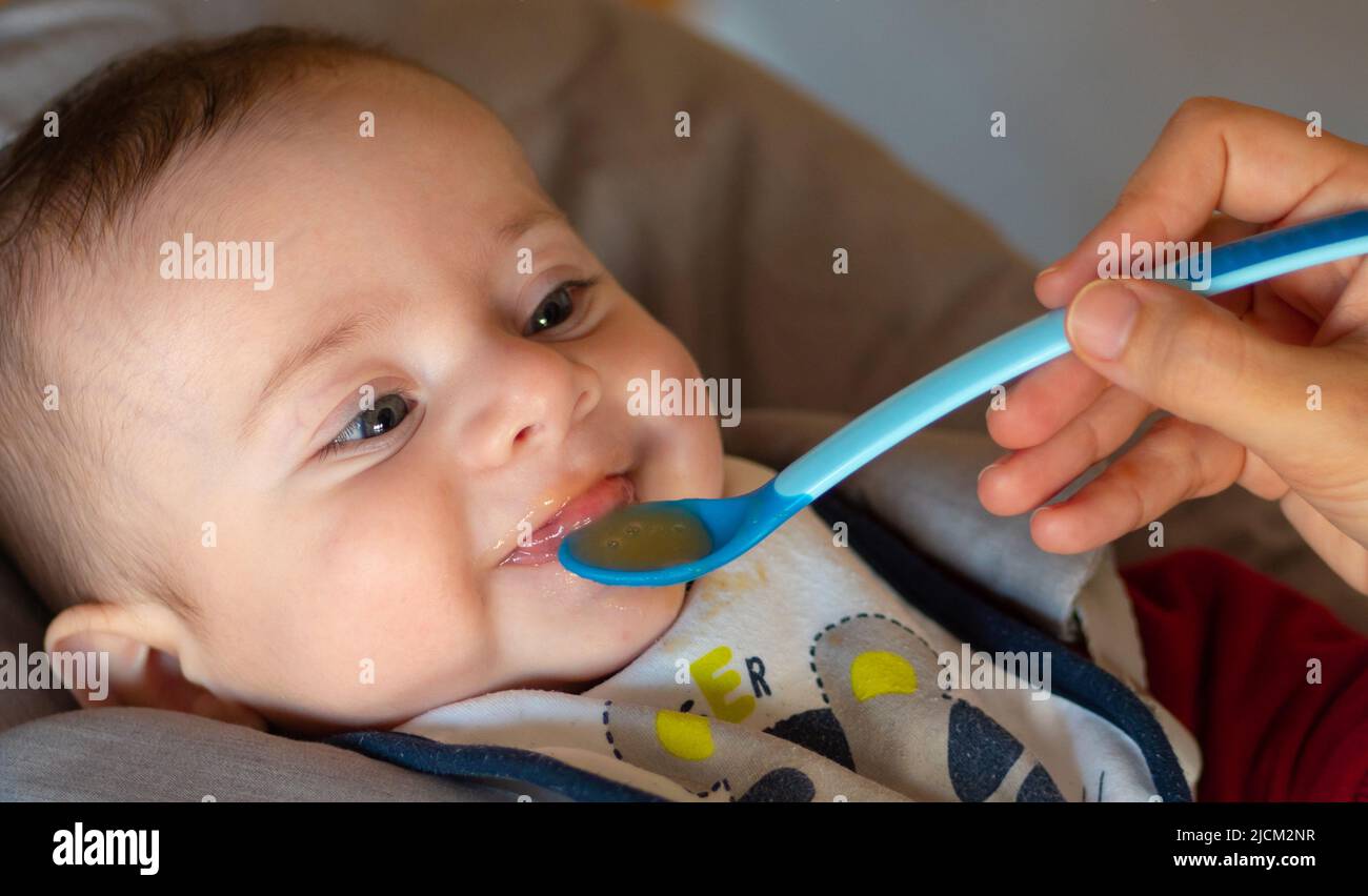 Close-up of a few months old baby starting weaning by eating a fruit puree. Stock Photo