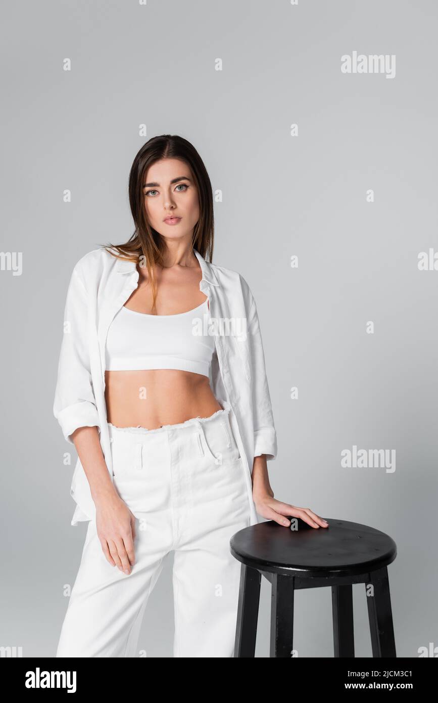 https://c8.alamy.com/comp/2JCM3C1/woman-in-white-bra-and-shirt-posing-near-black-stool-isolated-on-grey-2JCM3C1.jpg