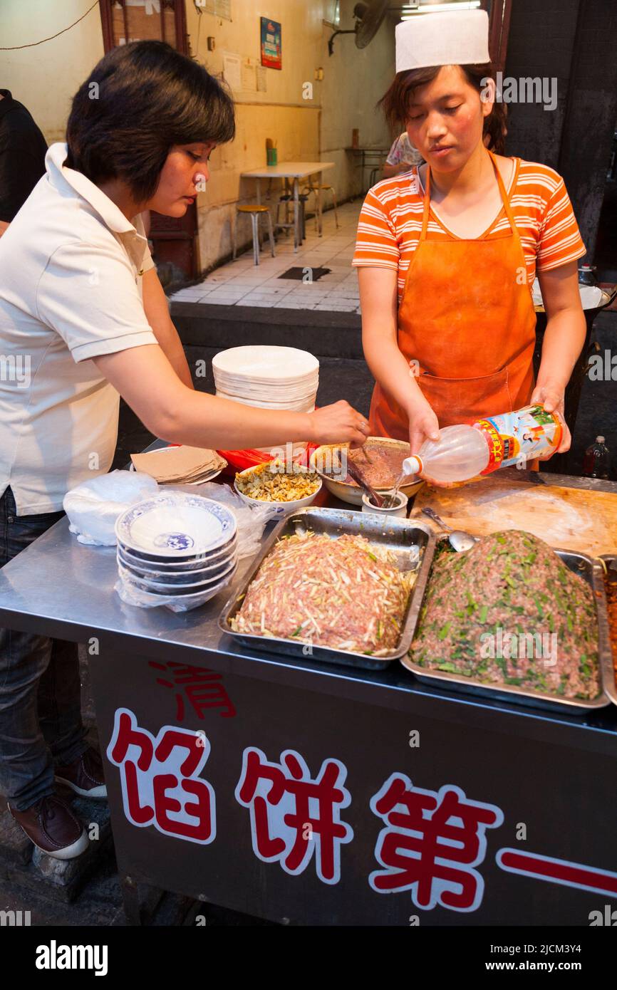 Women staff prepare cooked meat for pie filling type dishes in a local takeaway food restaurant kitchen serving / serves hot Chinese food to customers to eat. Xi'an, China. (125) Stock Photo