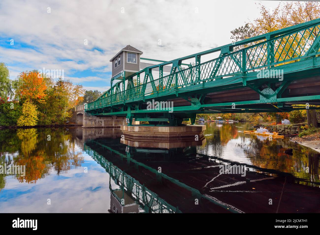 Swing bridge across a river on a partly cloudy autumn day. Reflection in water. Stock Photo