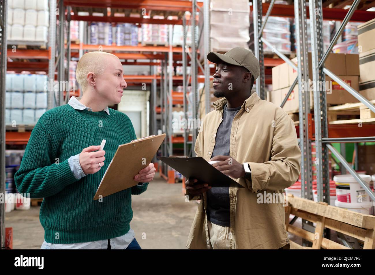 Two multiethnic colleagues talking to each other during work with transportation documents in warehouse Stock Photo