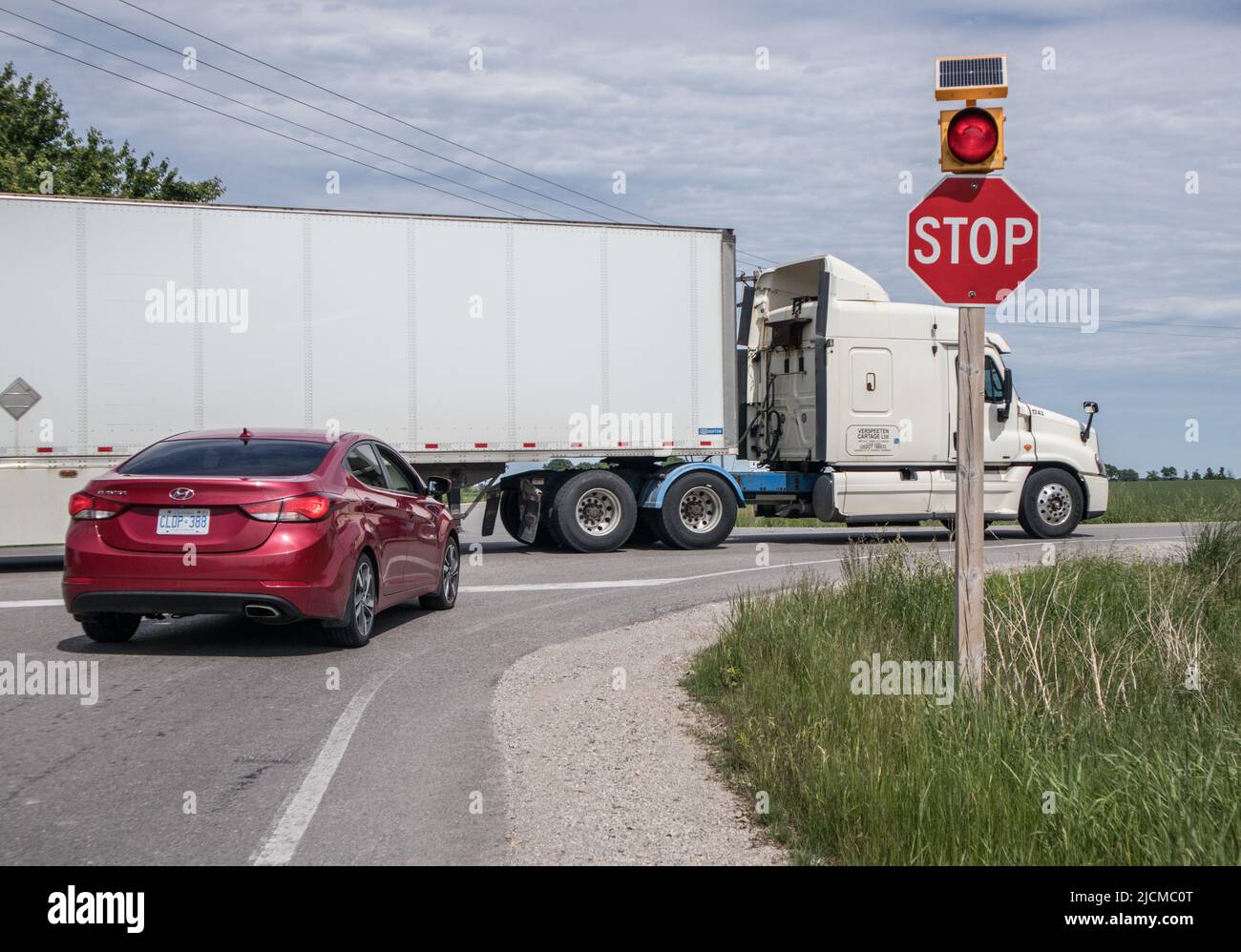 STOP signage with red light flashing, a big truck has priority. Stock Photo