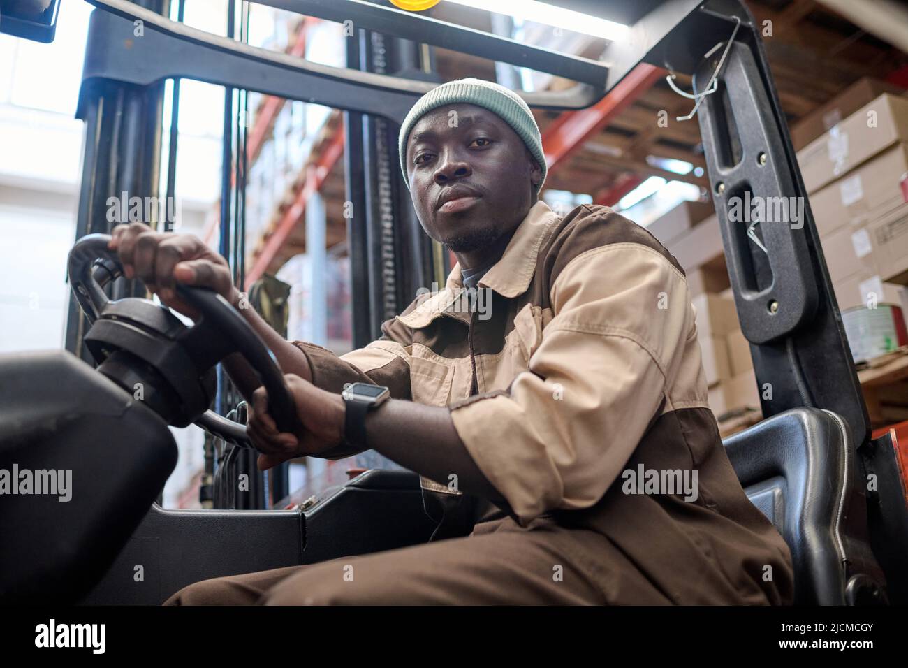 Portrait of African american driver looking at camera while driving forklift at warehouse Stock Photo