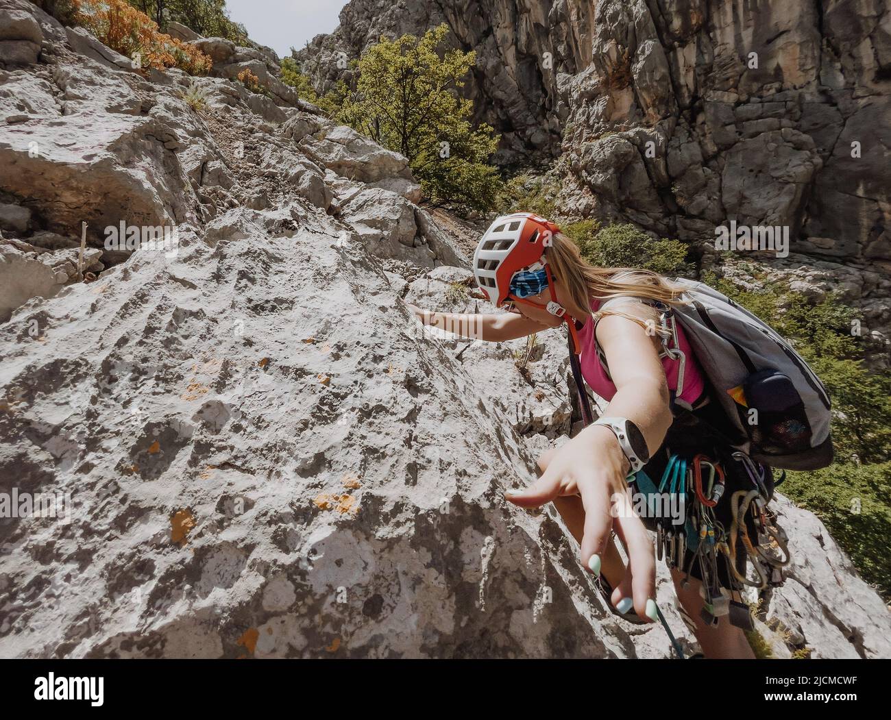 Athletic Woman in protective helmet and harness with rope and quickdraws climbing on cliff rock wall using in Paklenica National park site in Croatia. Stock Photo