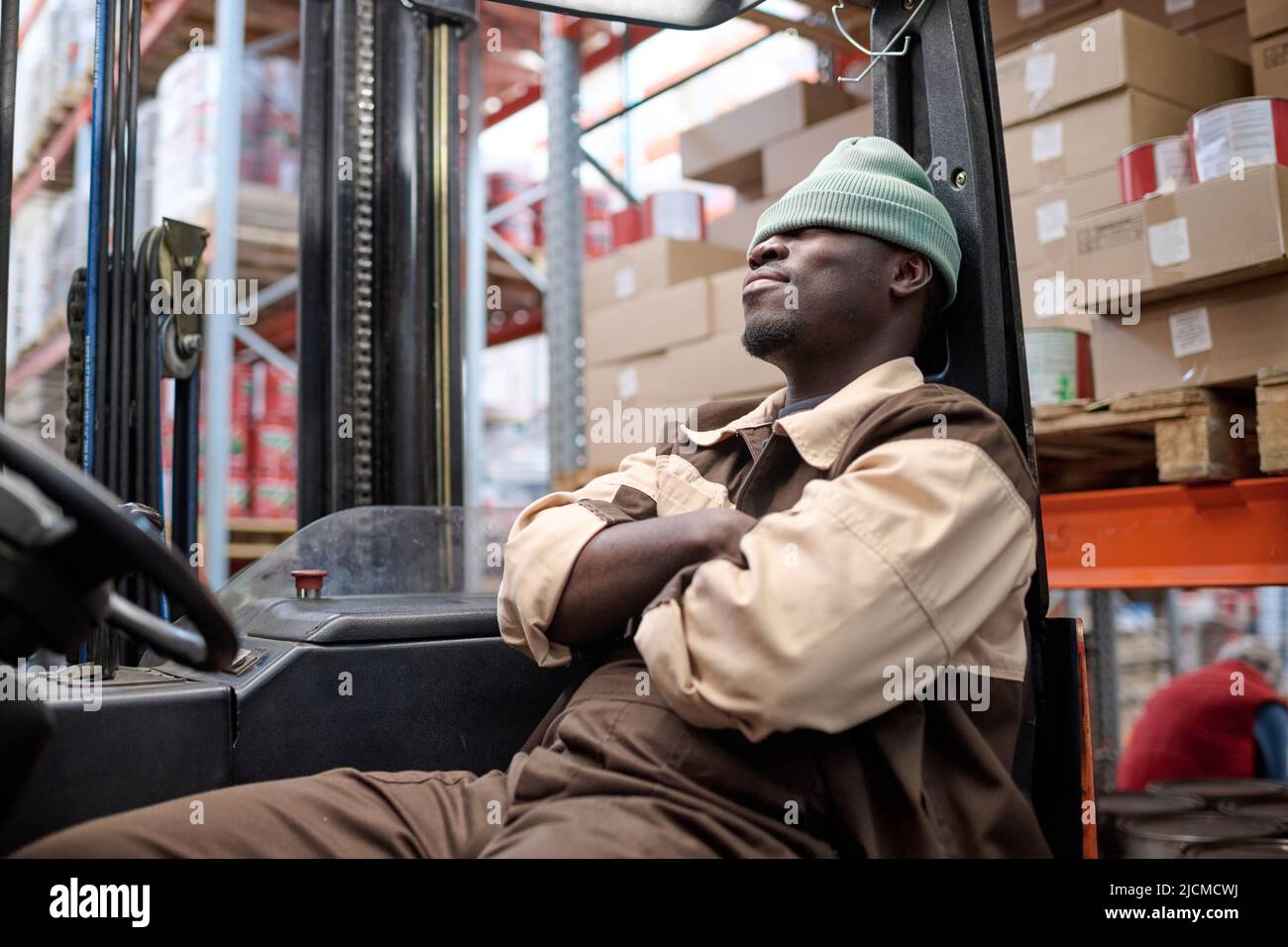 African young driver of forklift sitting on seat and relaxing after work at warehouse Stock Photo