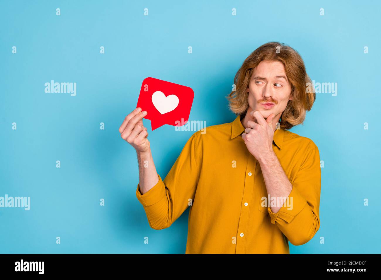 Portrait of attractive trendy skeptic long-haired guy holding like card deciding isolated over bright blue color background Stock Photo