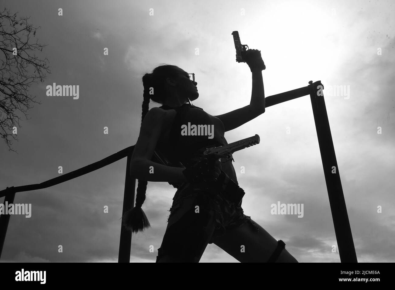 A young woman is seen posing as a silhouette figure of her cosplay action superhero Lara Croft. Stock Photo