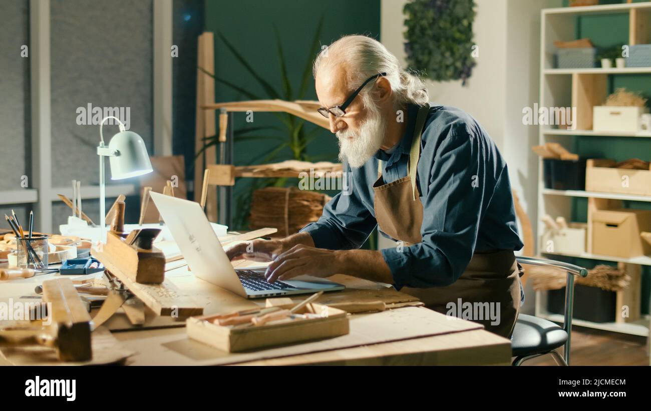 A Focused Carpenter Develops Layouts from Wood, Models 3D Sketches Using a Laptop in a Home