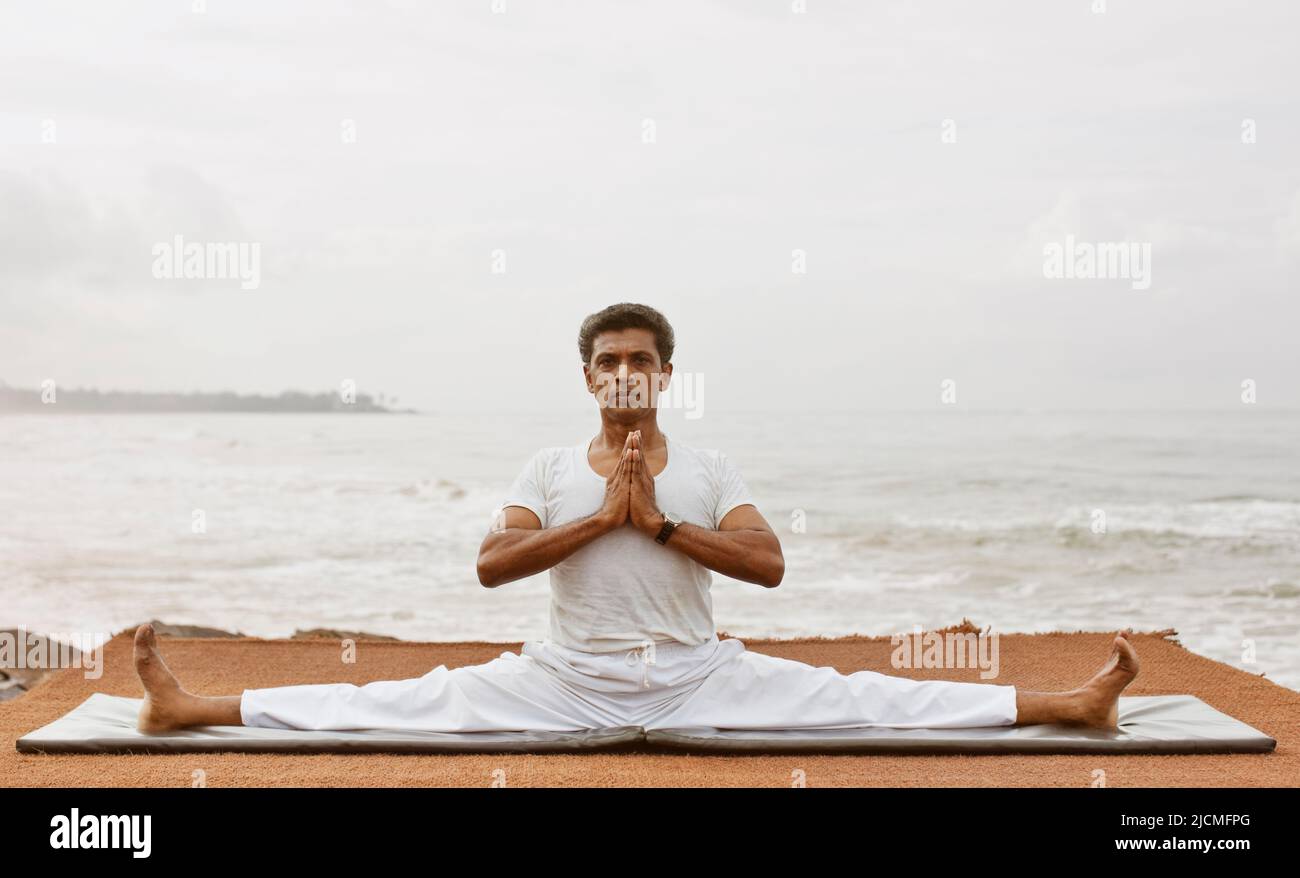 Sri Lankan yoga master practices yoga by the beach. Aturuwella, Bentota, Sri Lanka; shown here is the seated wide-legged straddle pose Stock Photo