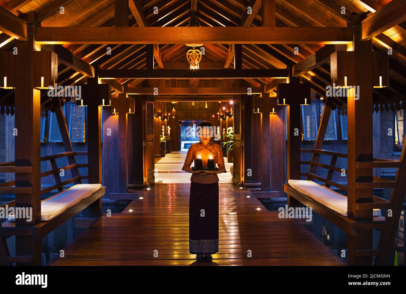 A young Asian female hotel staff member welcomes guests with a tray of candles at dusk at the entrance of a hotel, Siem Reap, Cambodia. Stock Photo
