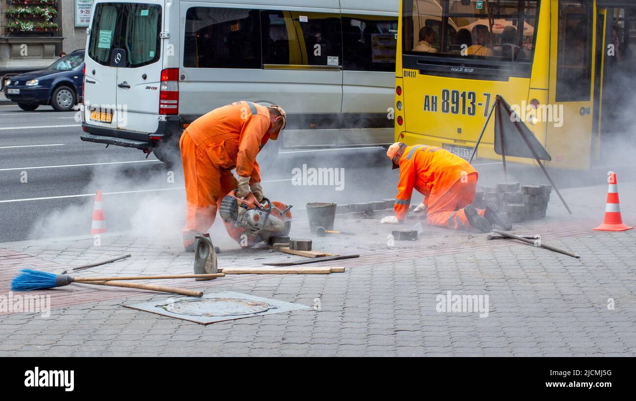 Road workers lay paving slabs. One with a circular saw cuts concrete blocks. Stock Photo