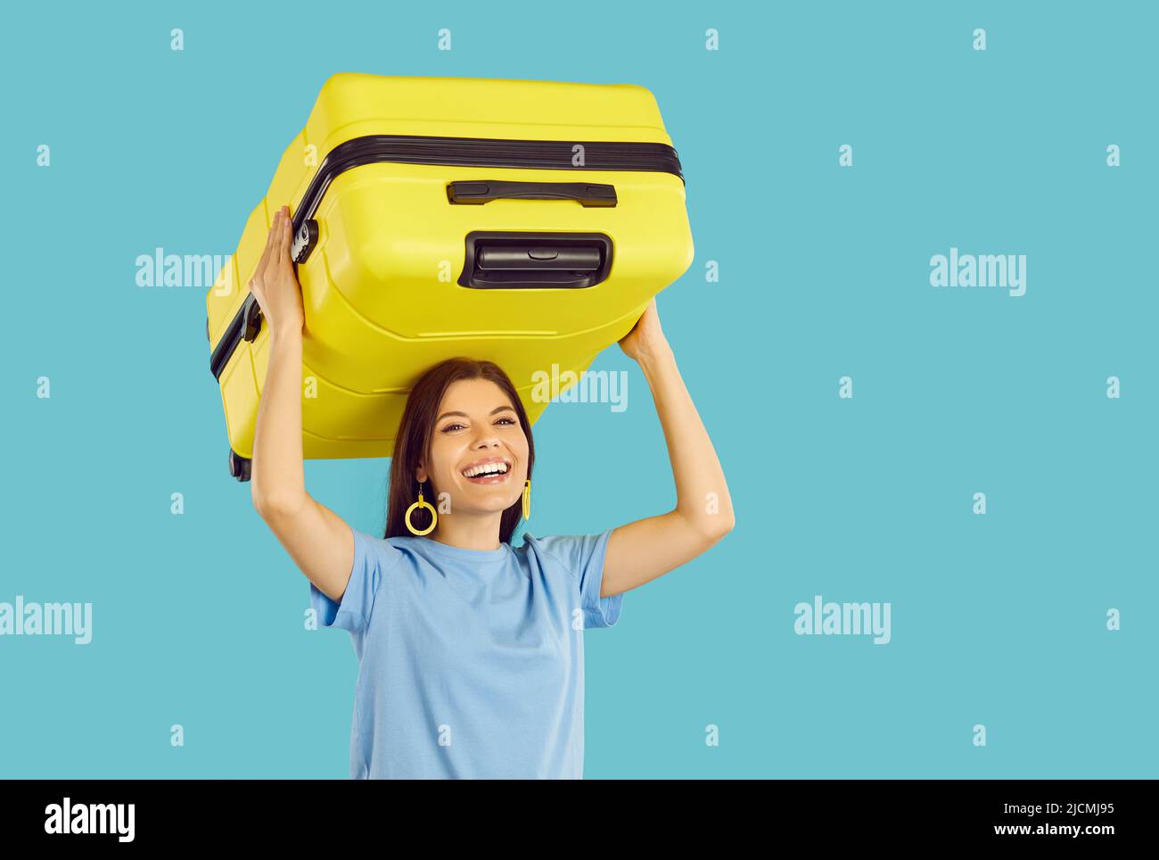 Cheerful woman who is going on holiday trip is carrying her yellow suitcase and laughing Stock Photo
