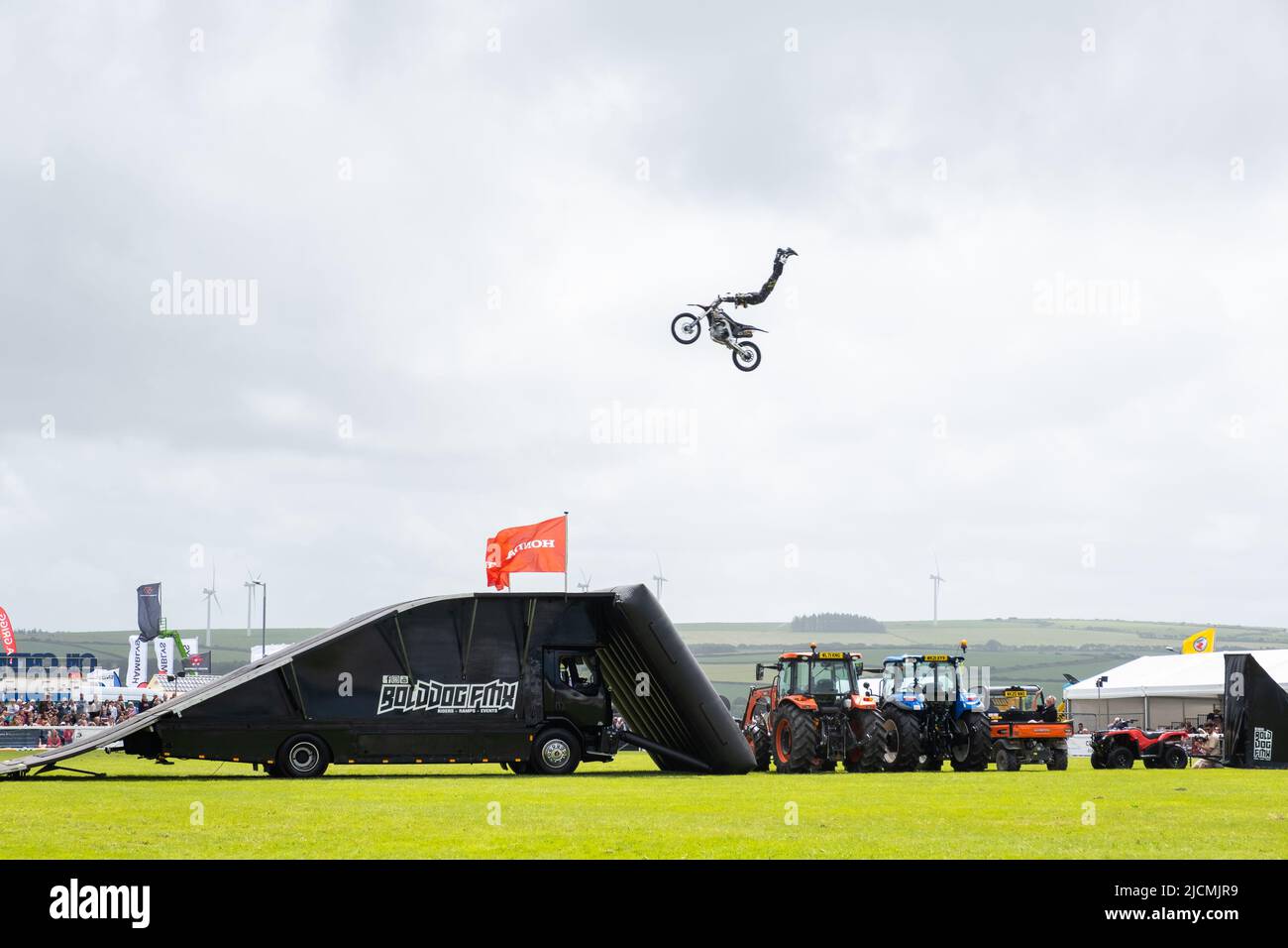 Members of the Bolddog FMX motorcycle stunt riding team riding at speed to clear tractors and slopes whilst doing amazing dangerous arial stunt tricks Stock Photo
