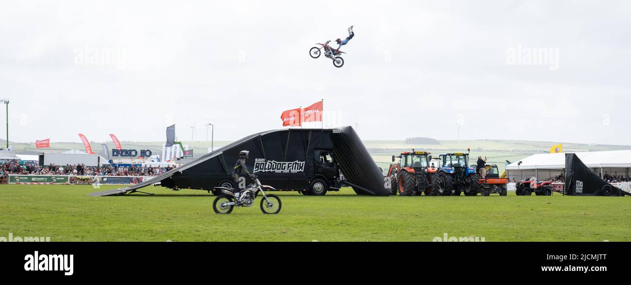 Members of the Bolddog FMX motorcycle stunt riding team riding at speed to clear tractors and slopes whilst doing amazing dangerous arial stunt tricks Stock Photo
