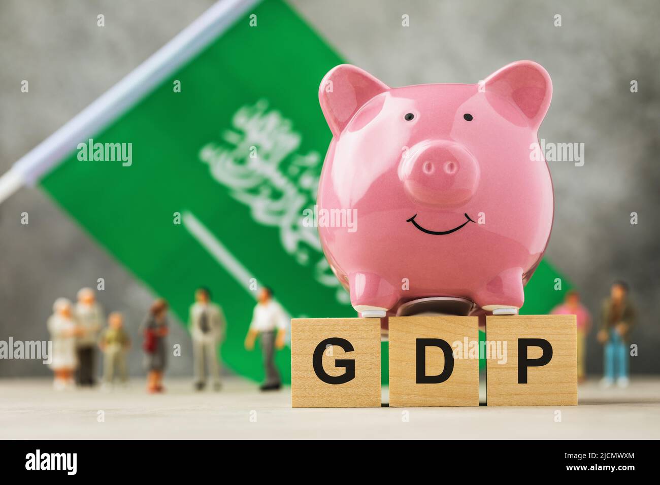 Piggy bank, wooden cubes with text, toy people made of plastic and a flag on an abstract background, a concept on the theme of the GDP of Saudi Arabia Stock Photo