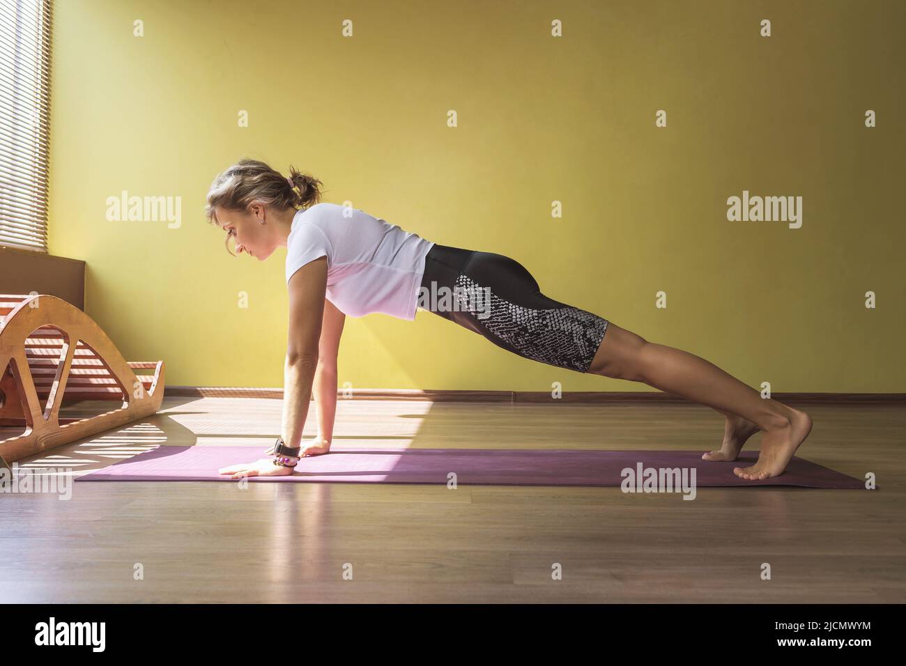 Woman in sportswear practicing yoga doing kumbhakasana exercise, plank pose, exercising on mat in room Stock Photo