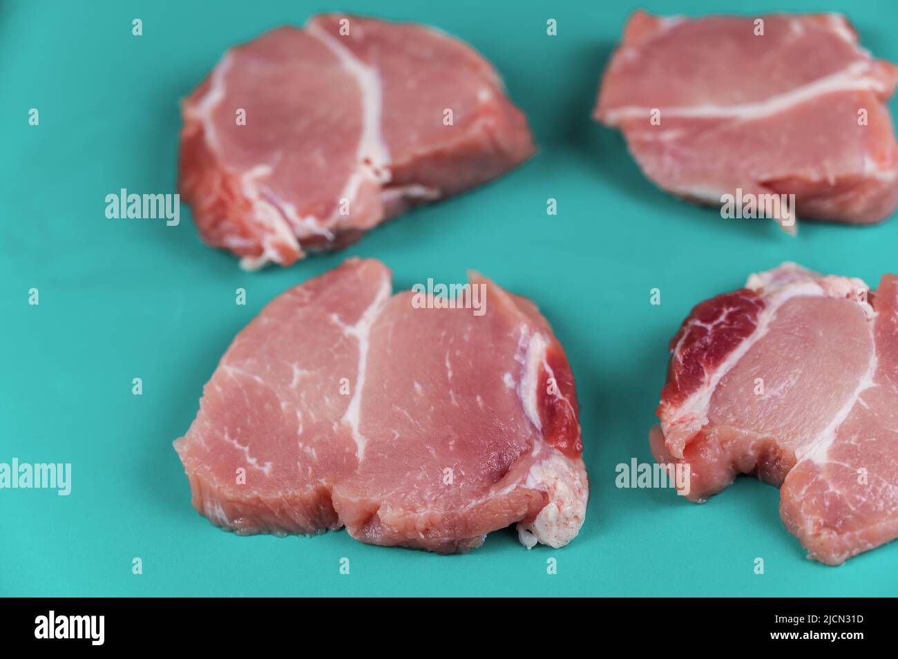 Raw pork opposite turquoise background. Four portioned pieces of pork