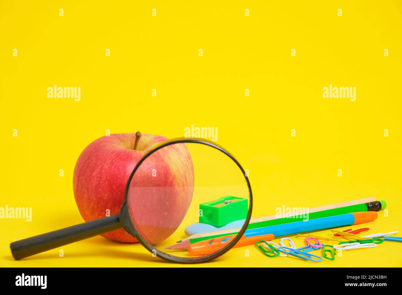 Apple, magnifying glass and school stationery yellow background Stock