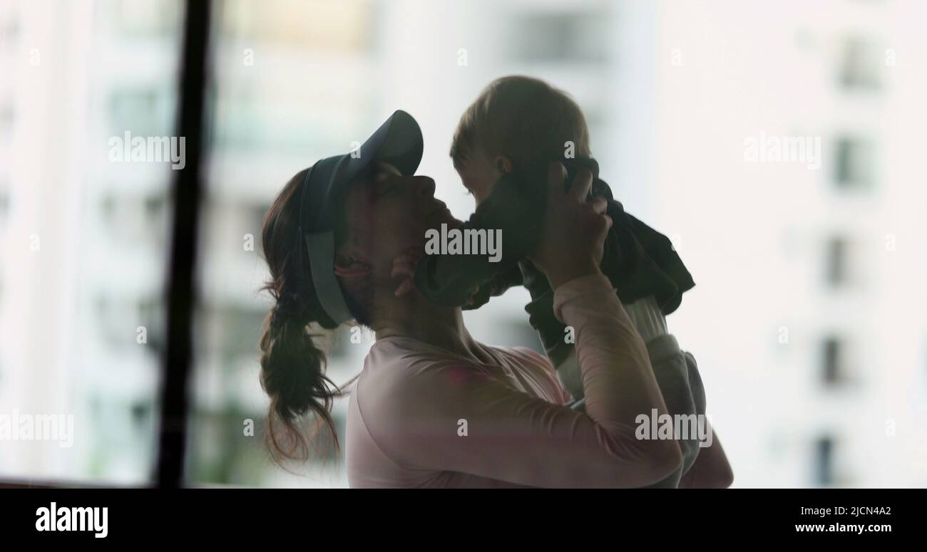 Silhouette of mother picking up baby in arms loving relationship. Mom