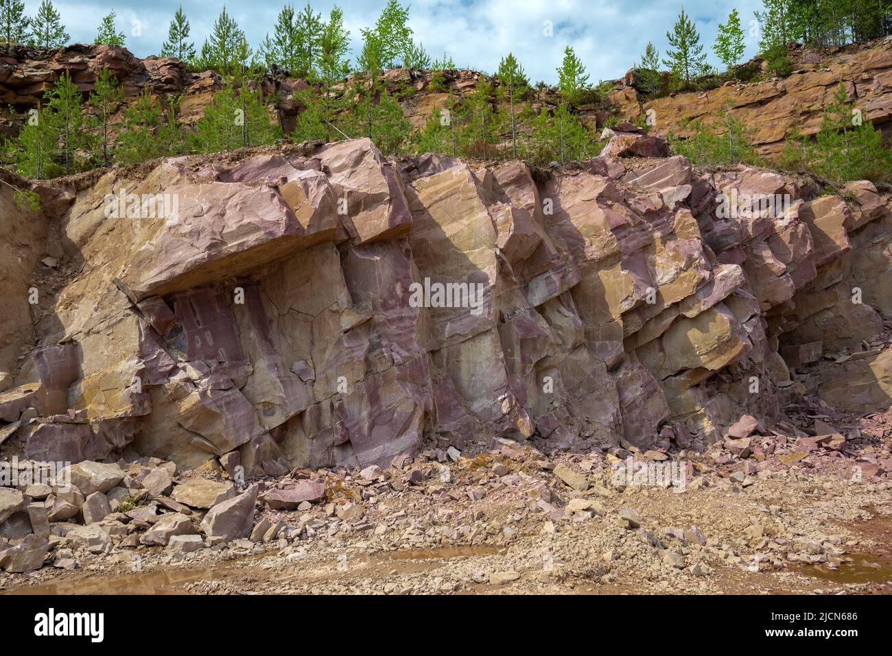 A section of crimson quartzite rock in an old quarry. Kvartsitny village, Karelia Stock Photo