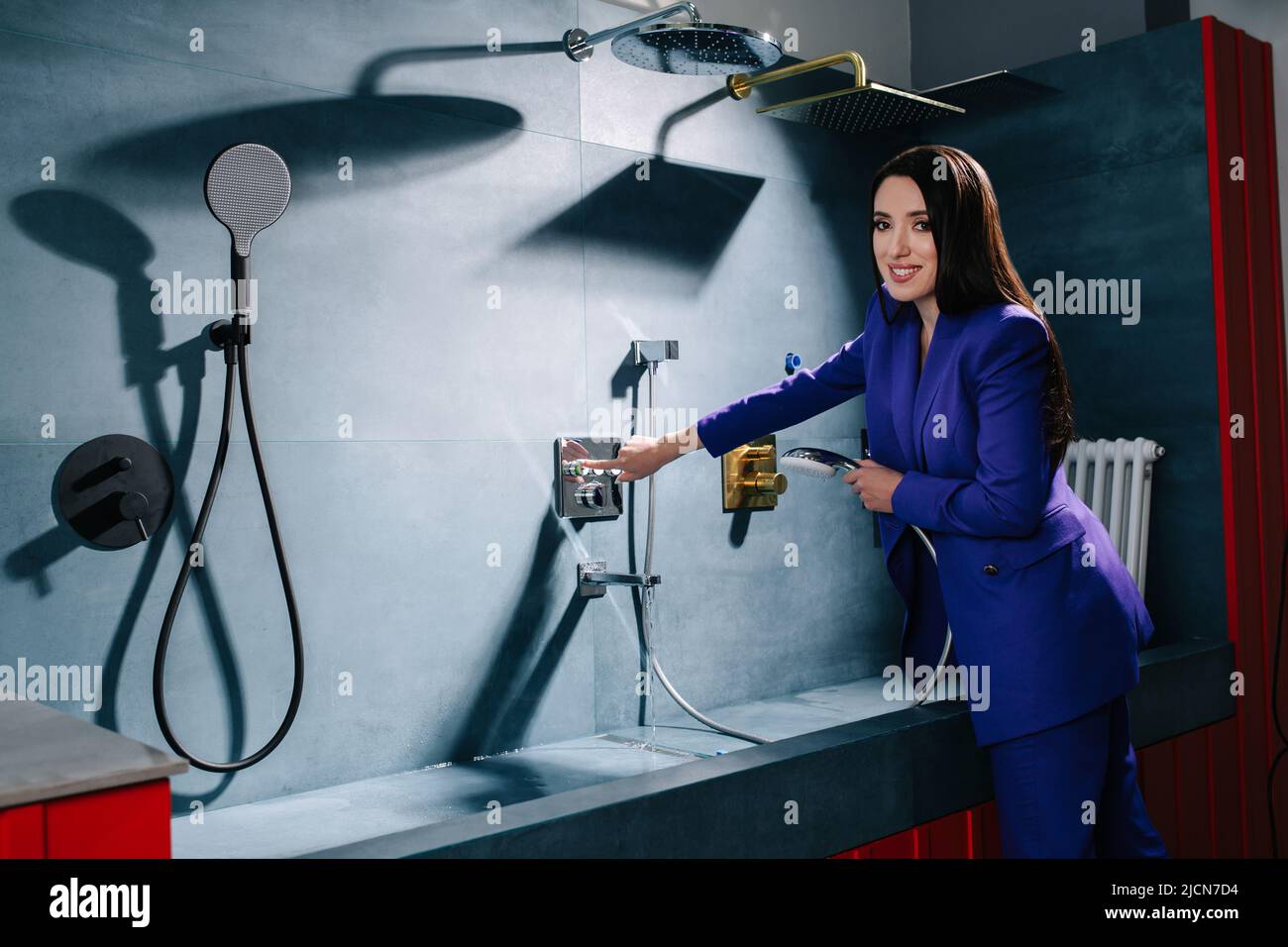 Saleswoman in a purple suit testing a showerhead, looking at the camera Stock Photo