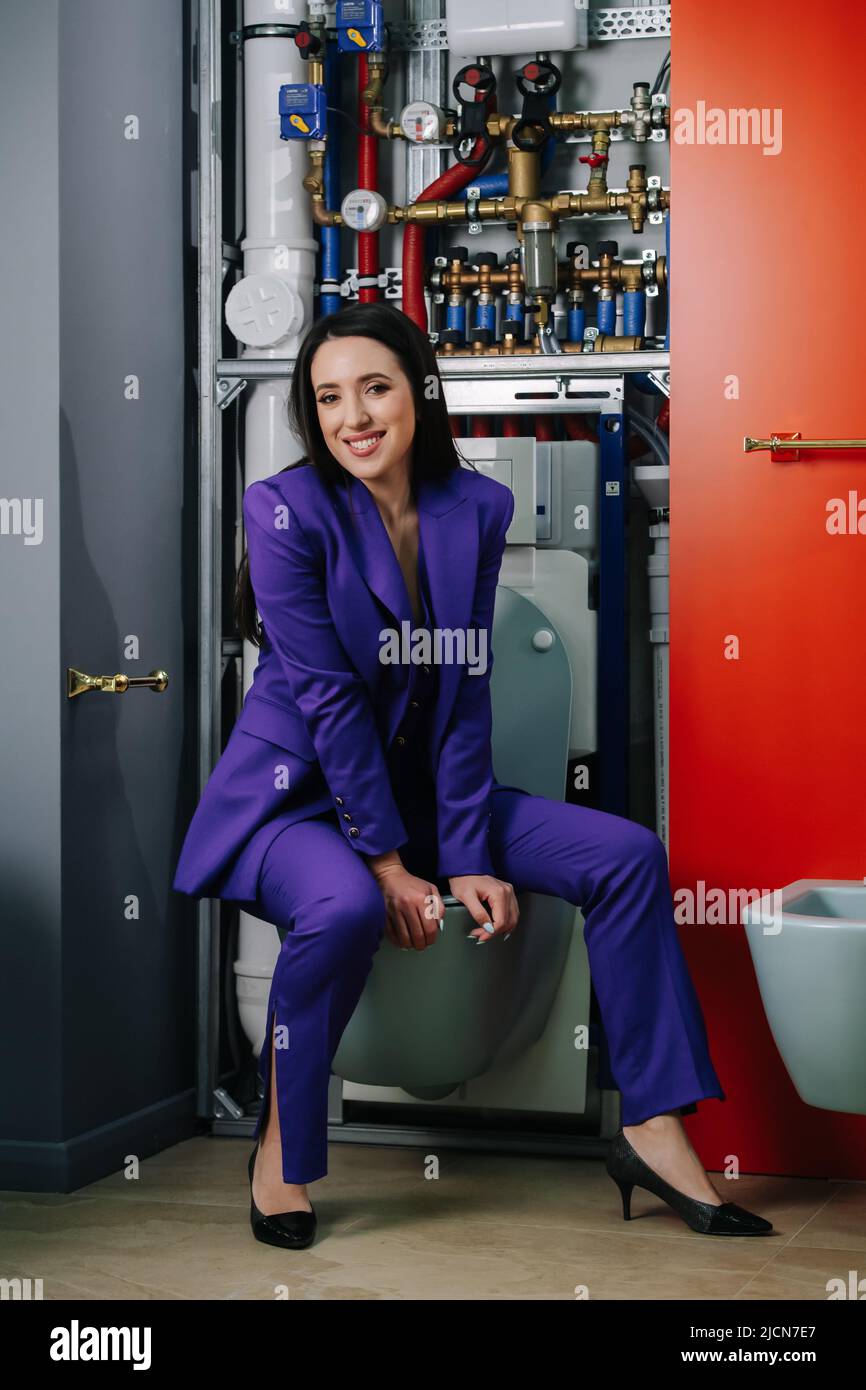 Sitting on a toilet saleswoman in a purple suit presenting plumbing options Stock Photo