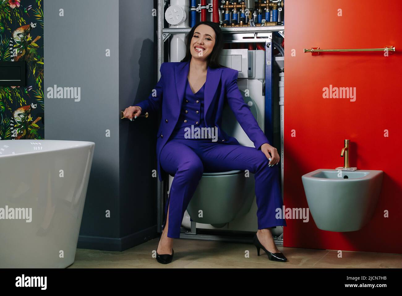 Giggling, sitting on a toilet saleswoman presenting plumbing options Stock Photo