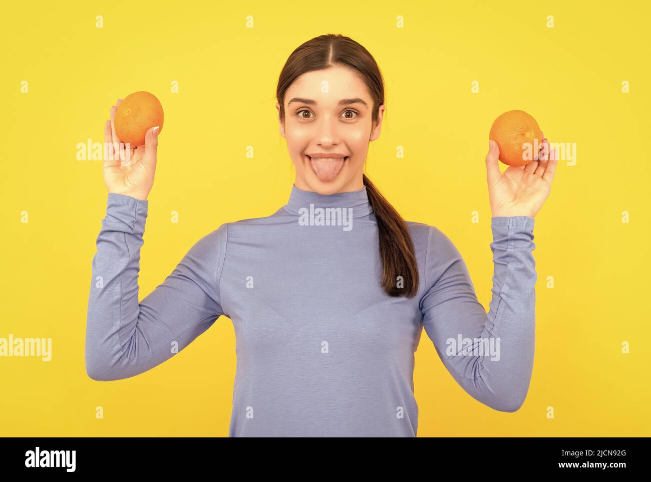 happy young woman holding orange citrus fruit on yellow background, organic Stock Photo