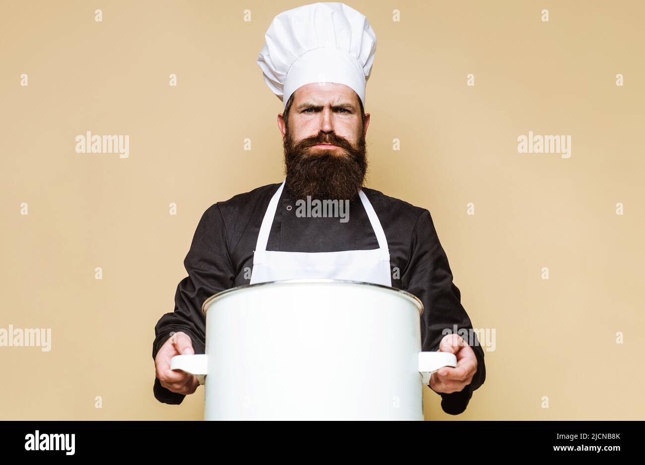 Bearded chef in uniform with big saucepan or pot. Cooking utensils. Kitchenware. Food preparation. Stock Photo