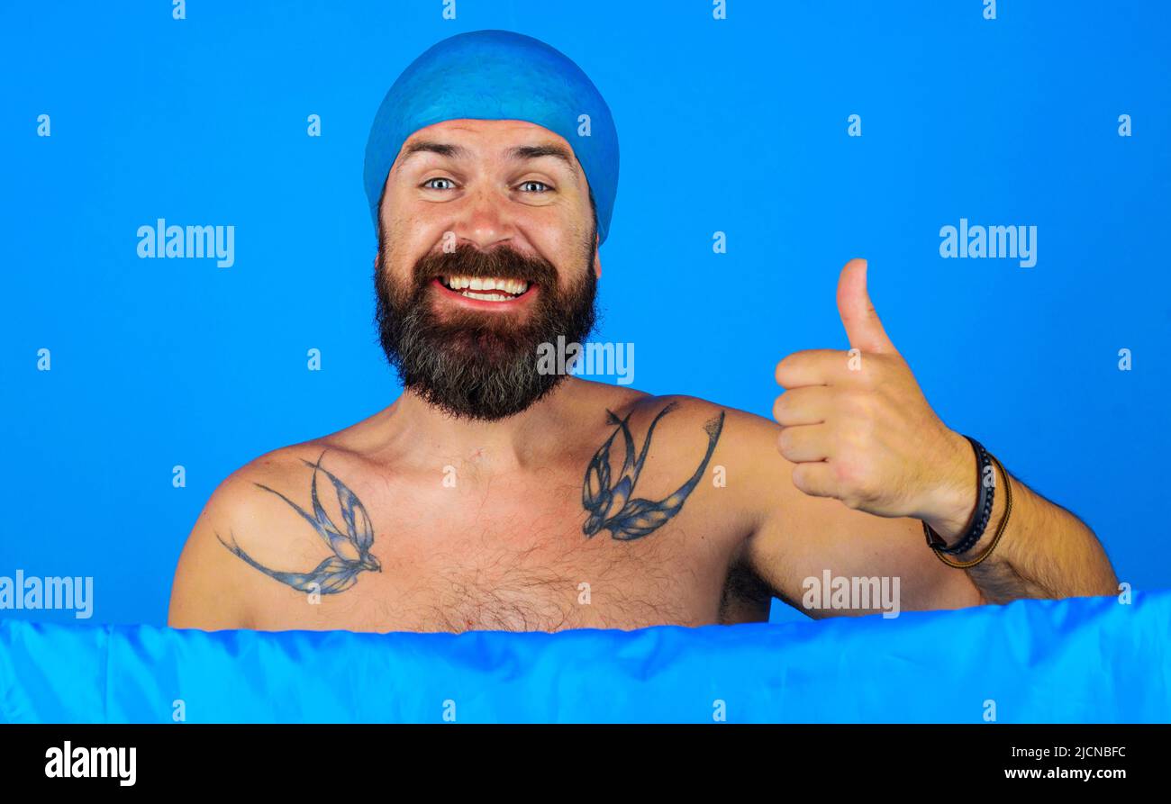 Happy bearded man in shower cap on head shows thumb up. Bath time. Showering and washing. Good mood. Stock Photo