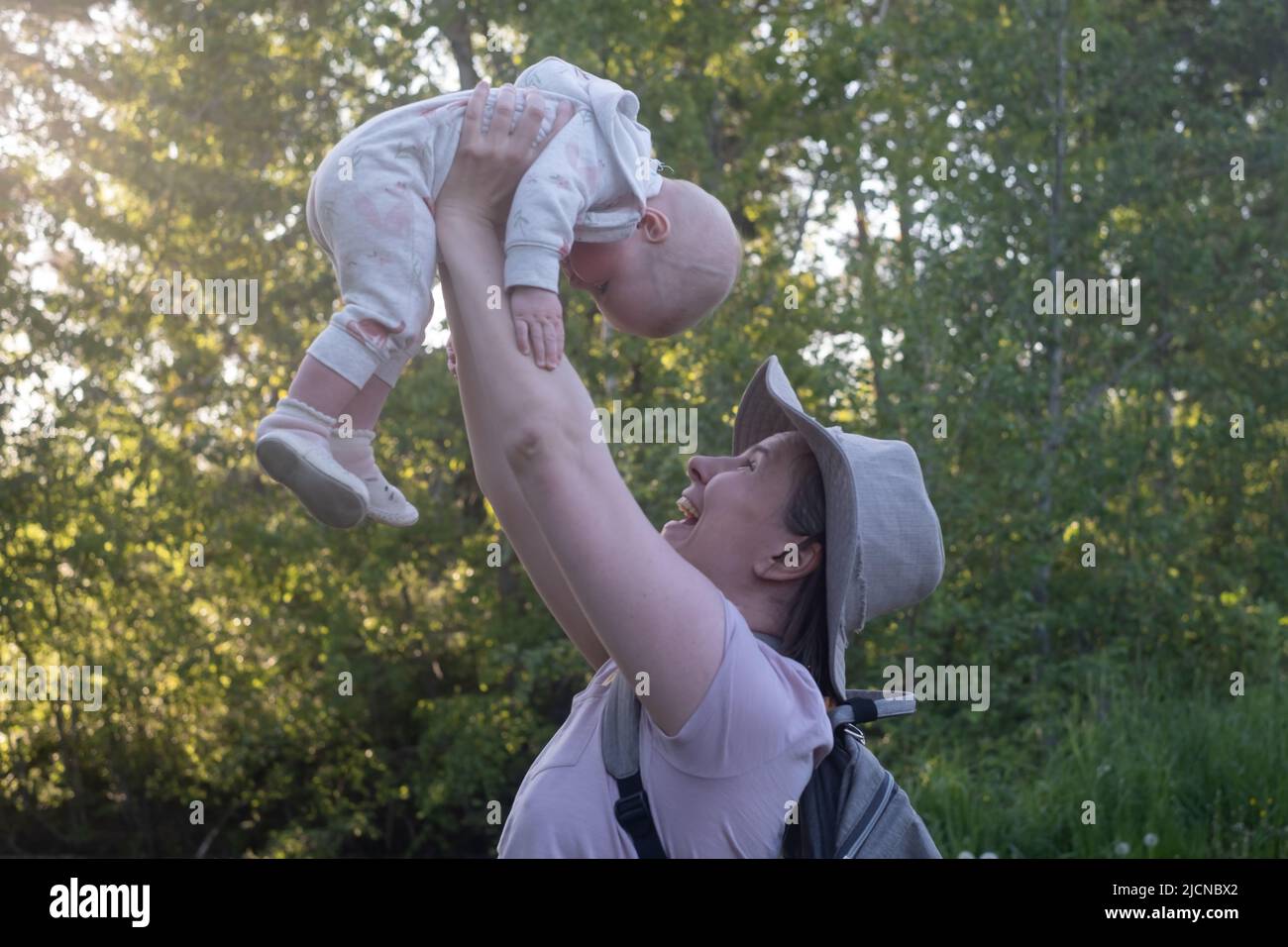 Young mother throws up baby in the sky, summer outdoors. Happy mom and ...