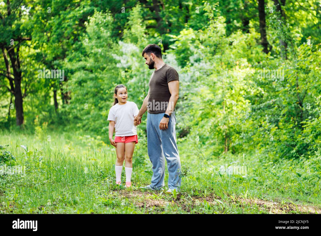 Portrait of wonderful family walking in forest around trees. Little daughter holding hand of father. Summer activities. Stock Photo